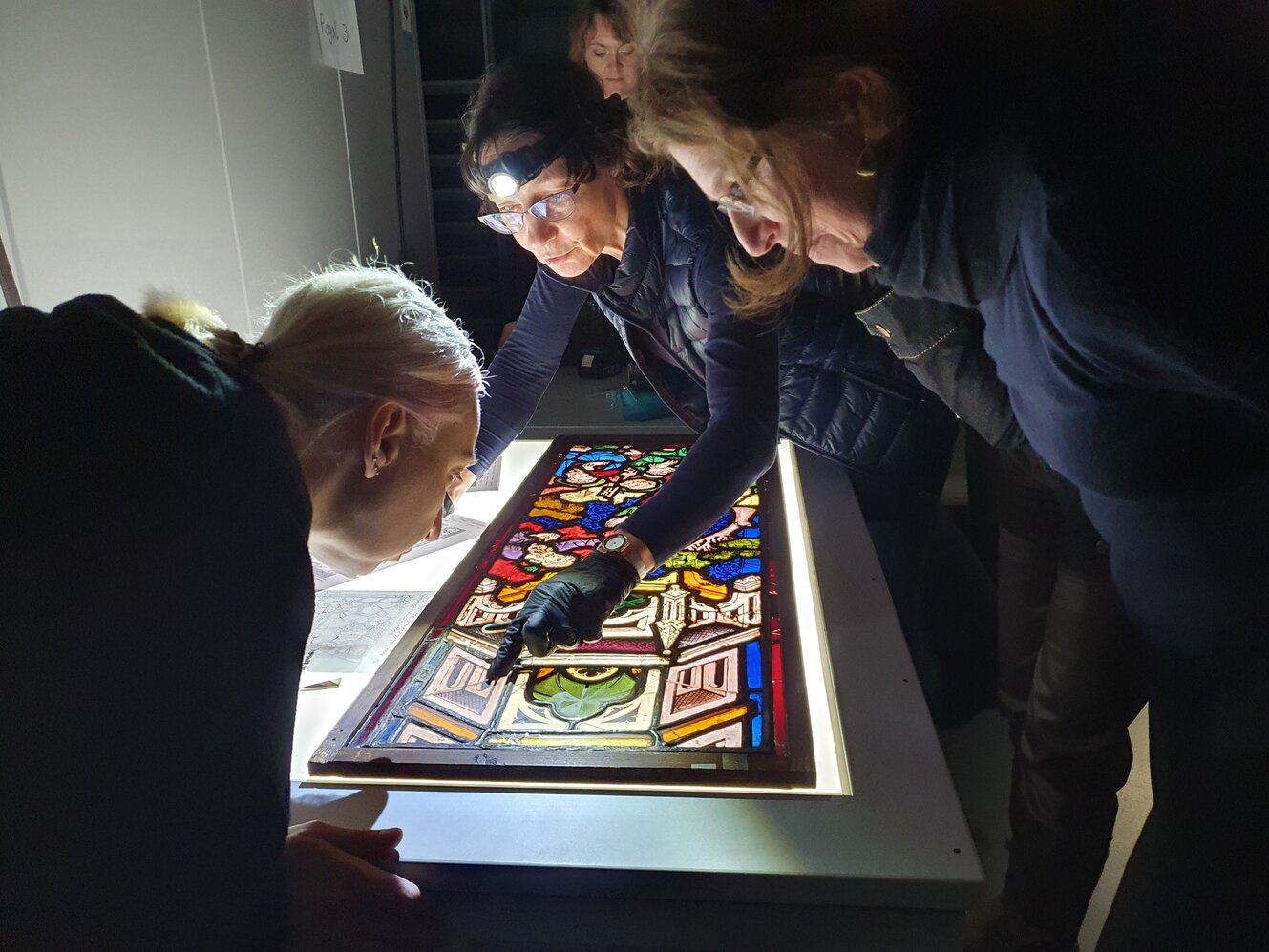 Mehrere Personen betrachten ein Glasfenster, das auf einem Leuchttisch liegt