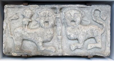Steinrelief auf dem zwei stilisierte Löwen zu sehen sind. Sie wenden den Kopf dem Betrachter zu.