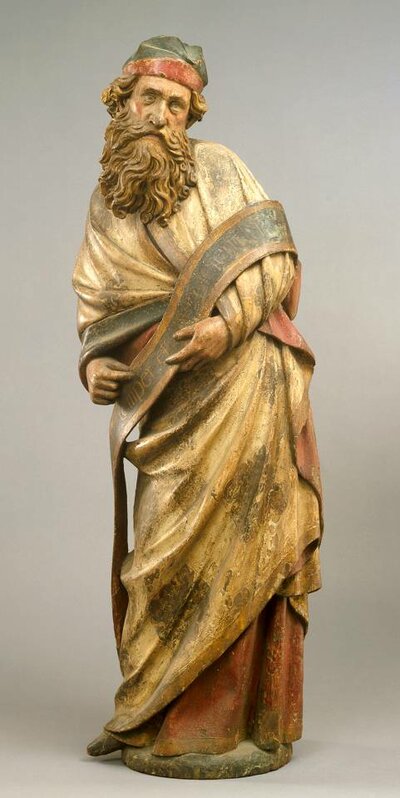 Figur eines stehenden Mannes mit vollem Bart. In seinen Händen hält er einen Schlal mit Inschrift.