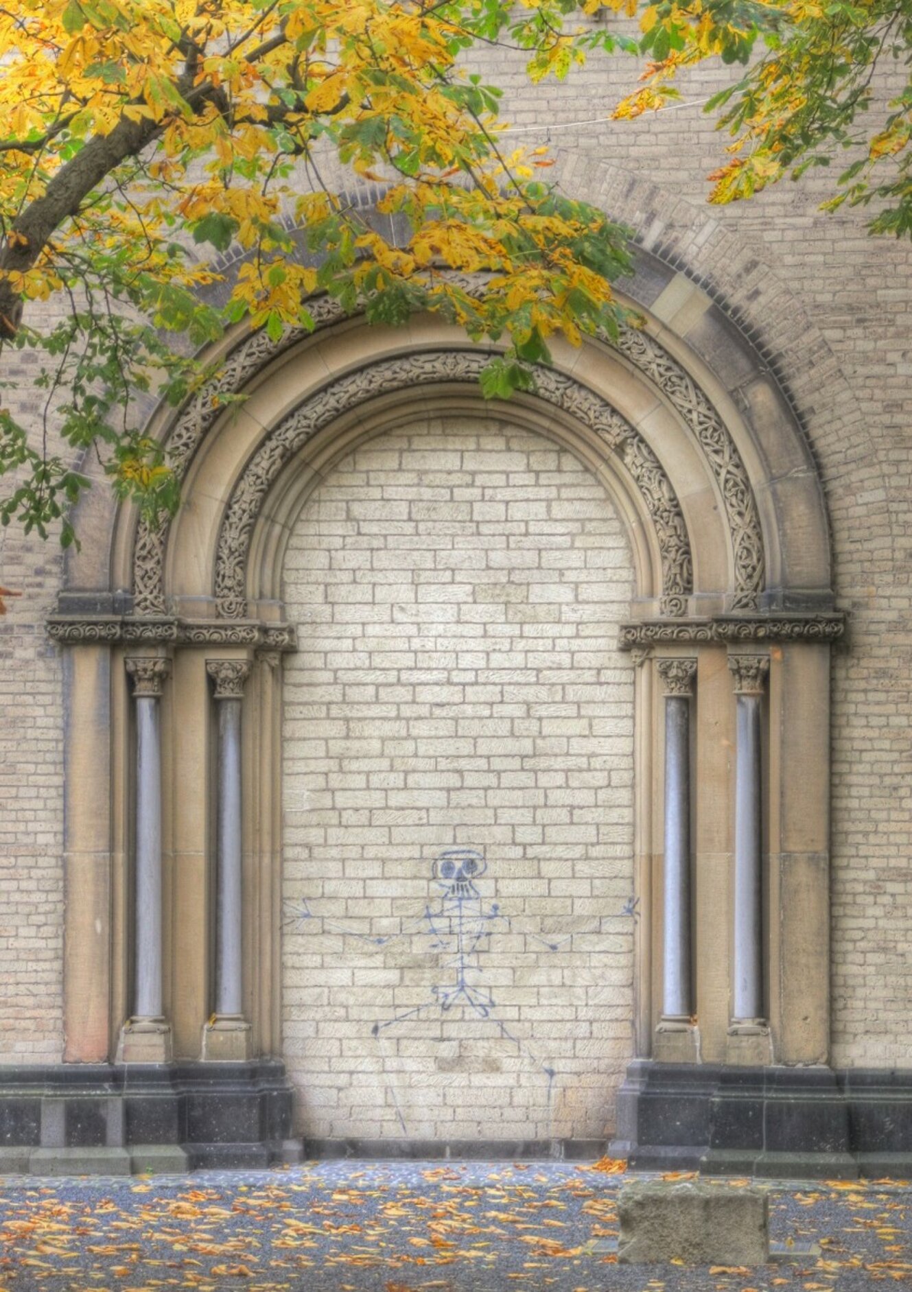 Graffito eines Knochenmanns an der Wand unter einem Steinbogen.