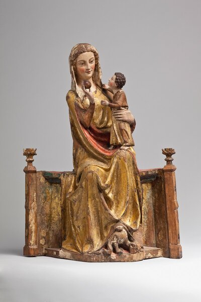 Holzfigur einer jungen Maria, die auf einem breiten Thronsitz sitzt. Auf ihrem Arm hält sie das Jesuskind. Sein Gesicht ist ihr zugewand.