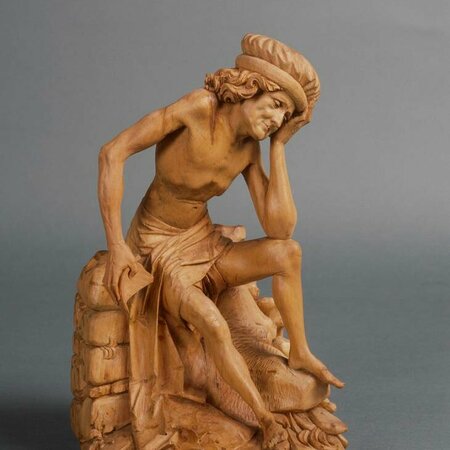 Holzfigur eines sitzenden Mannes. Seinen Kopf hat er in seine linke Hand gelegt. Sein Blick ist zum Boden gesenkt.