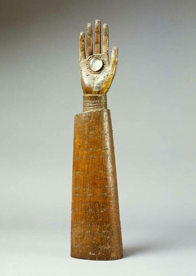 Aufrechter Arm aus Holz. In der Handinnenfläche ist ein runder Bergkristall eingefasst.