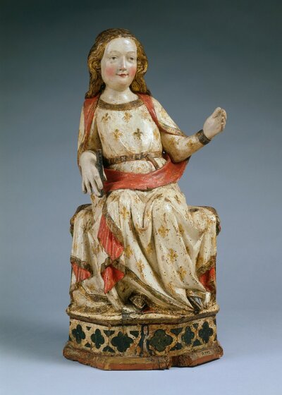 Lächelnde Maria, auf einem Thron sitzend; sie trägt ein weißes Gewand mit goldenen Lilien und rotem Saum, die Hand rechts hält einen kurzen schwarzen Stab, der Arm links ist angewinkelt und weist von ihr weg, die Hand ist geöffnet.