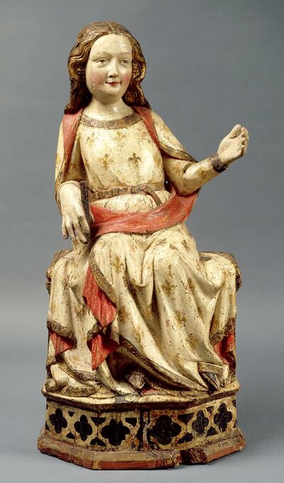 Lächelnde Maria, auf einem Thron sitzend; sie trägt ein weißes Gewand mit goldenen Lilien und rotem Saum, die Hand rechts hält einen kurzen schwarzen Stab, der Arm links ist angewinkelt und weist von ihr weg, die Hand ist geöffnet.