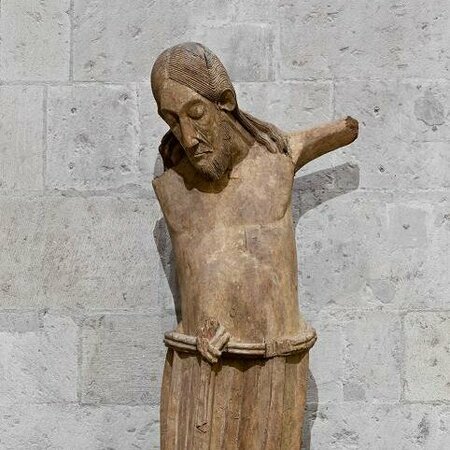 Holzskulptur eines Mannes. Sein Kopf ist geneigt, die Augen geschlossen. Die Figur besitzt keine Arme und Füße.