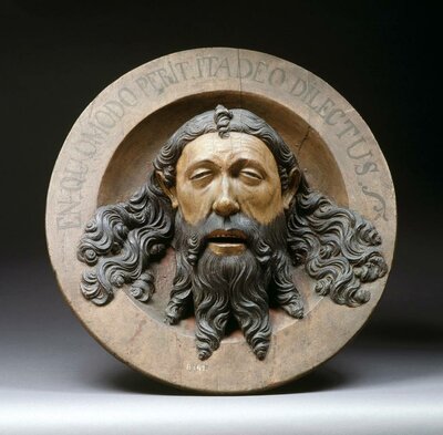 EIne runde Holzschüssel mit dem geschnitzten Gesicht eines bärtigen Mannes in der Mitte. Die Inschrift am oberen Rand der Schüssel lautet: In quomodo perit, ita deus dilectus.