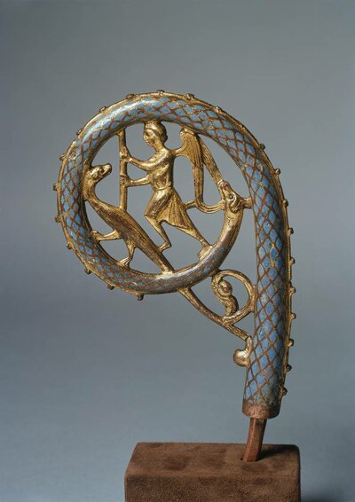 Oberes Ende eines Bischofsstabs. Die Rundung ist blau mit goldener Einfassung und Verzierung. Innerhalb der Rundung befinden sich die Figur eines Engels und eines Tieres auf zwei Pfoten.