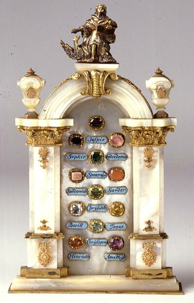 Barock anmutendes Miniaturtor aus Permutt mit bronzener Verzierung und in der Mitte verschiedenen geschliffenen Edelsteinen mit blauen Schildern zur Bezeichnung darunter