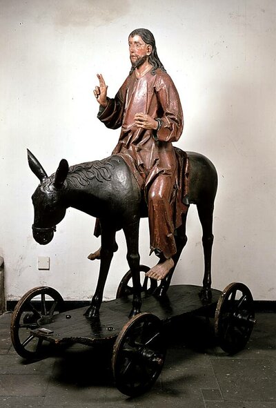 Eine Christusfigur sitzt auf einem Esel. Dieser steht auf einem Karren.