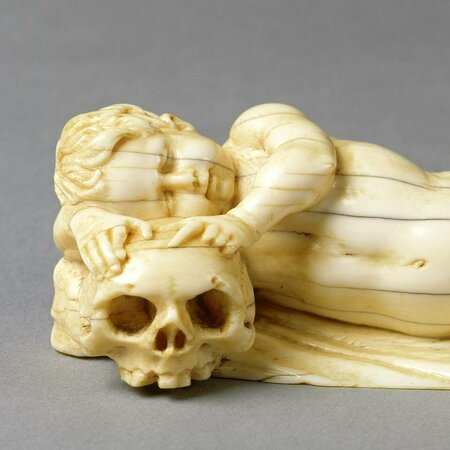 Im Liegen schlafender Putto. Wie auf einem Kissen liegt sein Kopf auf einem Totenschädel.