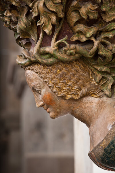 Weibliche Büste mit einem Wappen auf der Brust und einem Kopfschmuck aus geflochtenen Reben.