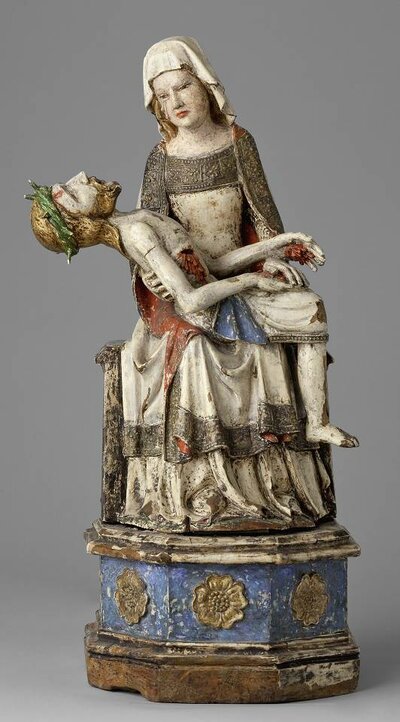 Sitzende Maria aus Holz. Sie trägt ein weißes Kleid und hat den Kopf trauernd gesenkt. Auf ihrem Schoß liegt der tote Jesus mit Dornenkrone.