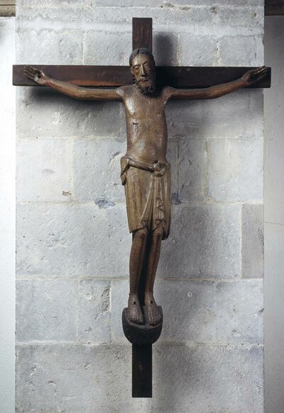 Holzfigur, die Jesus am Kreuz darstellt. Sein Kopf ist geneigt, die Augen halb geschlossen.