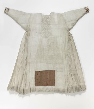 Weißes Gewand mit Stickereien an den Ärmeln und rechteckigen Verzierung auf der Vorderseite.