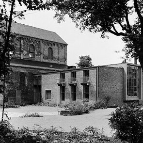 Schwarz-weiß Fotografie eines rechteckigen Baus neben einem kirchlich anmutendem Gebäude.