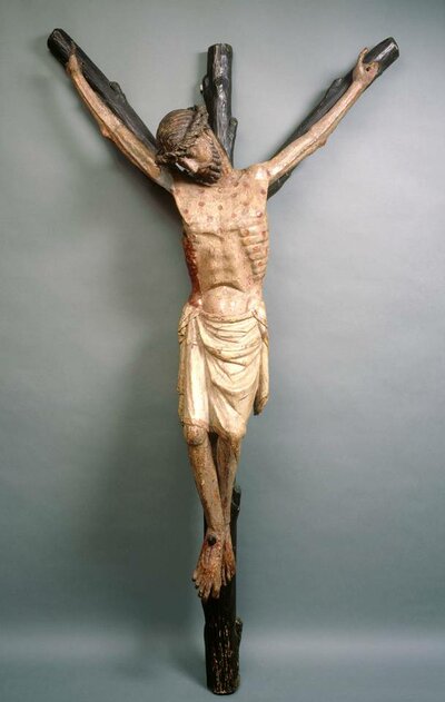 Kruzifix aus Holz. Das Kreuz ist als Baumstamm mit Ästen dargestellt. Die rechte Hand von Jesus fehlt.