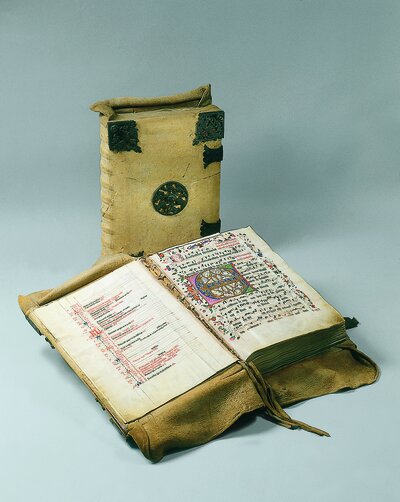 Ein aufgeschlagenes Buch liegt vor einem geschlossenen Buch mit hellem Einband. Die Seiten zeigen Text, der jedoch nicht zu lesen ist.