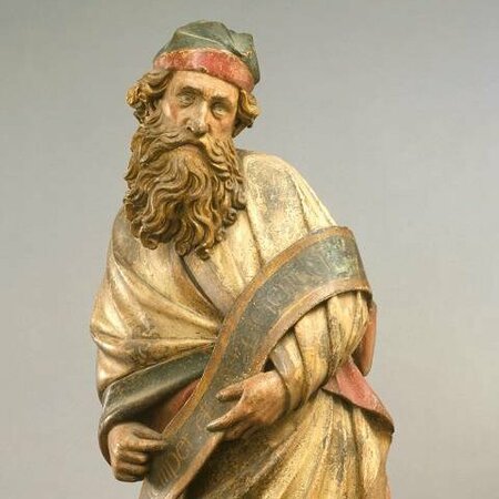 Figur eines stehenden Mannes mit vollem Bart. In seinen Händen hält er einen Schlal mit Inschrift.