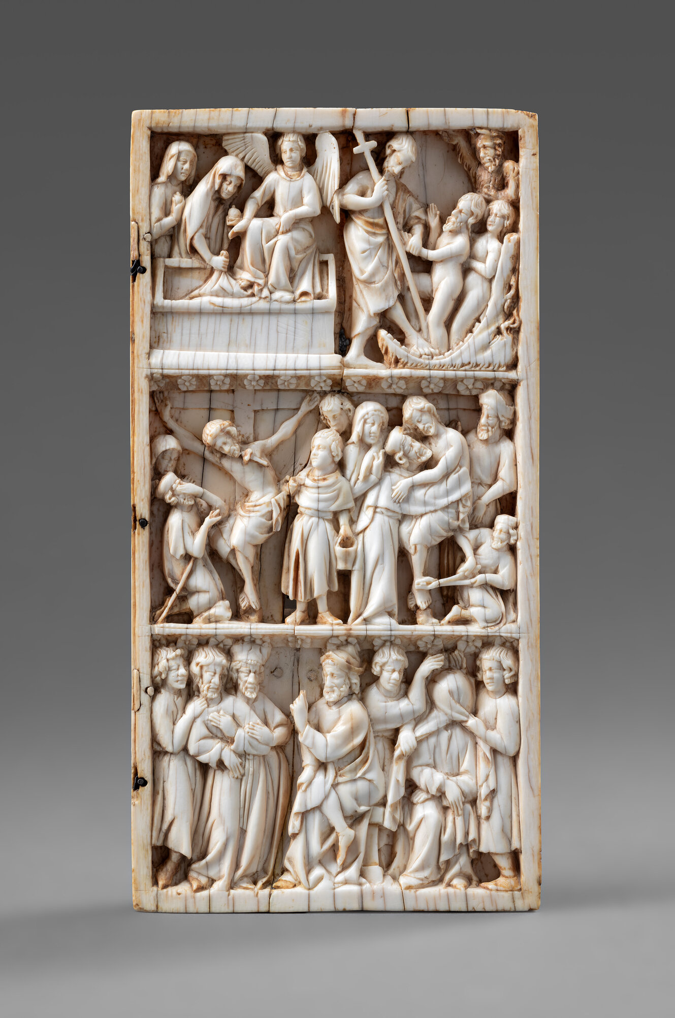 Rechteckige Elfenbeinschnitzerei mit drei Unterteilungen. Oben: Menschen an einem offenen Sarkophag, ein Engel und ein Mann mit einem Kreuz; in der Mitte: Jesus am Kreuz von Trauernden umgeben; unten: verschiedene Menschen