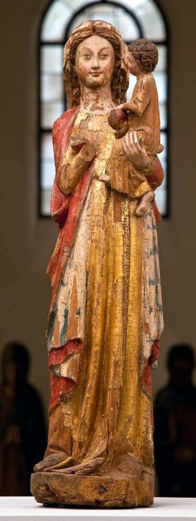 Stehende Madonna in einem goldenen Gewand und einem roten Mantel mit dem sitzenden Jesukind auf dem linken Arm. Das Kind blickt auf das Gesicht Marias, Maria blickt auf den Betrachter. Die rechte Hand der Madonna fehlt.