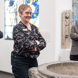 Eine Mitarbeiterin des Museum Schnütgen steht vor dem Taufbecken, welches sich in der Ausstellung befindet.