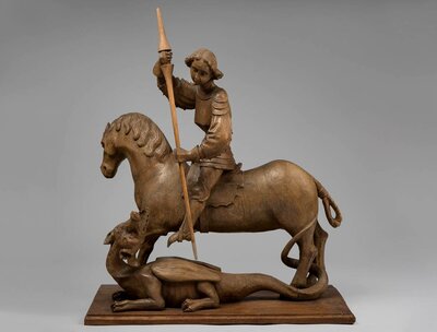 Holzfigur eines Ritters, der auf einem Pferd sitzt. Er sticht seine Lanze in einen liegenden Drachen.