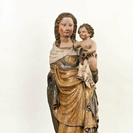 Holzfigur einer stehenden Maria. Auf ihrem Arm hält sie das Jesuskind. Ihr Gewand ist braun bemalt.
