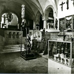 Schwarz-weiß Fotografie von einem Kircheraum, in dem verschiedene Objekte ausgestellt sind.