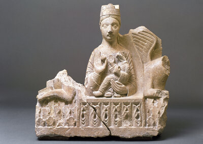 Steinskulptur der Maria mit Krone. Ihre rechte Hand ist gehoben, ihre linke Hand hält das Jesuskind. Die Abbildung ist nicht vollständig: An den Seiten ist der Stein abgebrochen.