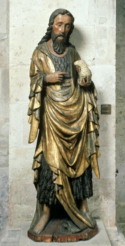 Holzfigur von Johannes dem Täufer. In seiner linken hand hält er ein kleines Schäfchen, auf das er mit seiner rechten Hand zeigt.