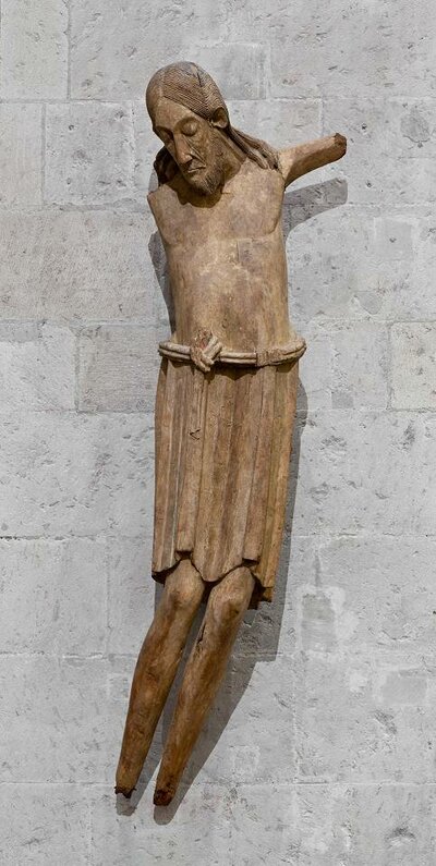 Holzfigur, die Jesus am Kreuz darstellt. Sein Kopf ist geneigt, die Augen halb geschlossen.