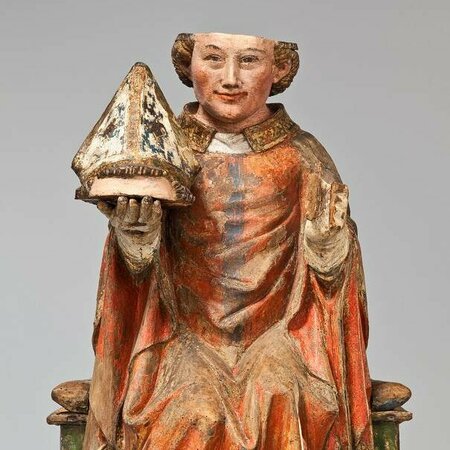 Holzfigur des Heiligen Dionysius. In seiner rechten Hand hält er seinen abgetrennten Skalp, auf dem ein Bischhofshut sitzt.