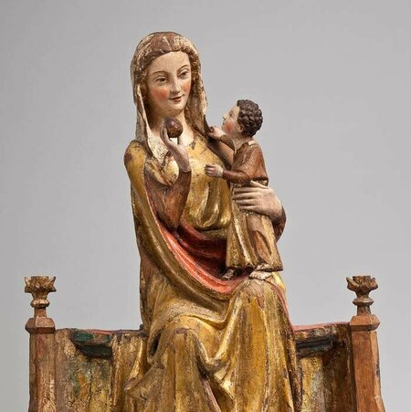 Holzfigur einer jungen Maria, die auf einem breiten Thronsitz sitzt. Auf ihrem Arm hält sie das Jesuskind. Sein Gesicht ist ihr zugewand.