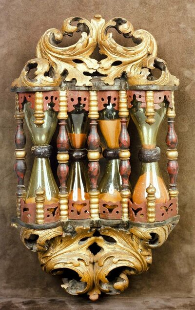 Kunstvoll geschnitzte Halterung mit vier Sanduhren. Diese sind mit bundem Sand befüllt.