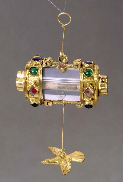 Vergoldetes Behälterchen mit buntem Glasbesatz. An der Unterseite hängt ein vergoldeter Vogel.