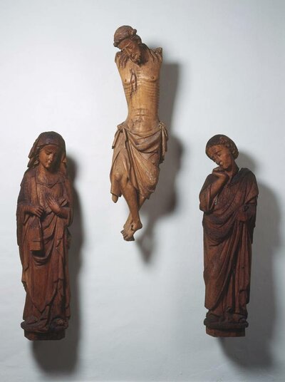 3 Holzfiguren, in der Mitte ein hängender Jesus ohne Kreuz und ohne Arme, links die trauernde Maria und rechts der trauernde Evangelist Johannes