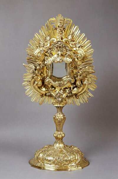 Vergoldetes und reich verziertes auf einem Ständer angebrachtes Schmuckgefäß mit einer gläsernen Schatulle für Hostien in der Mitte umrankt von Blumen und Ornamenten und mit Sonnenstrahlen umkränzt