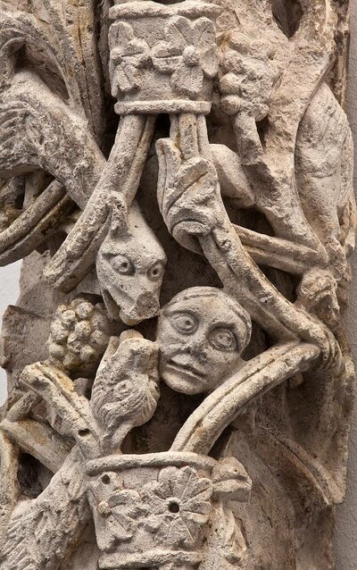 Ausschnitt eines größeren Objektes aus weißem Stein. Im Zentrum stehen zwei Drachenköpfe neben einem Menschenkopf.