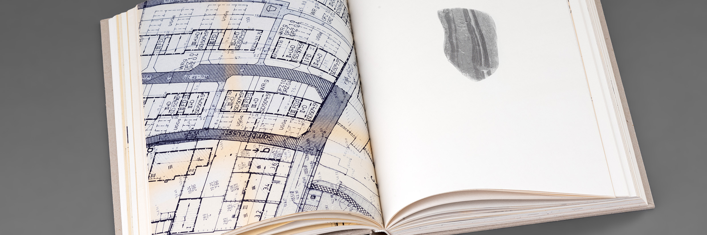 Aufgeschlagenes Buch mit einem Grundriss auf der linken Seite und der Abbildung eines bearbeiteten Steines auf der rechten Seite